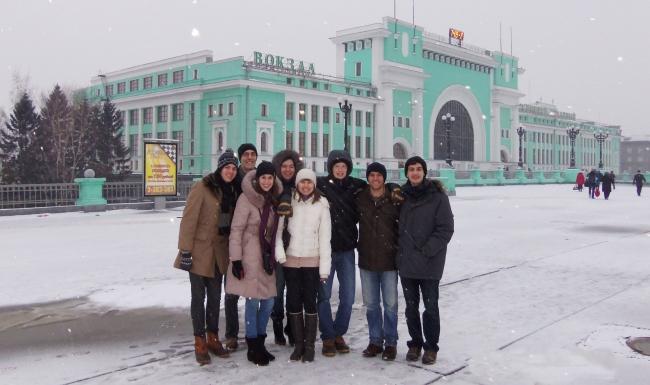 A group of students wearing coats and hats stand in front of an old train station