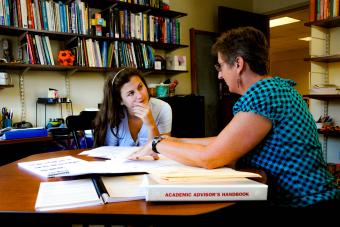 Prof. Molinek sits in her office with student looking at printed materials