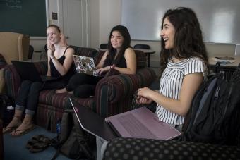 Three students smiling and talking to each other on a couch