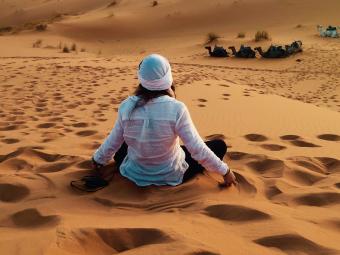Student sits on sand hill surrounded by desert facing away from the camera.
