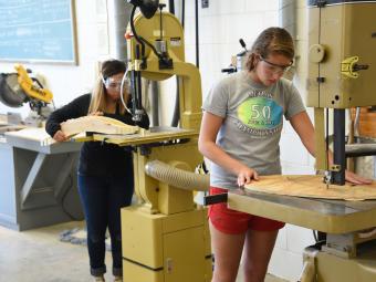 Two students work with machinery that cuts wood for a sculpture at the Sculpture Lab