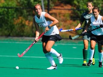 Field hockey game where two Davidson players and one competitor are running towards a ball