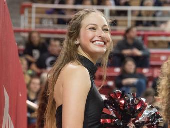 Cheeleader smiles and holds pom poms in Davidson colors during a basketball game