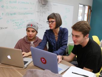 Prof Suzanne Churchill teaching with two students on laptop in classroom