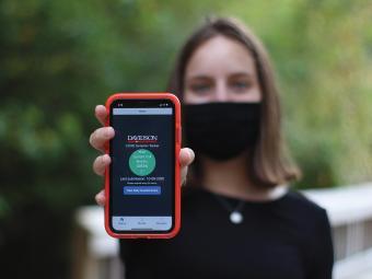 Student Holds Up Green Covid Symptom Tracker on her phone while wearing Mask