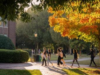 a group of students walking on a campus as sun sets and foliage is in the background