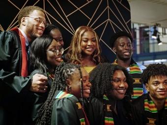 a group of young Black people in graduation regalia pose together for a photo