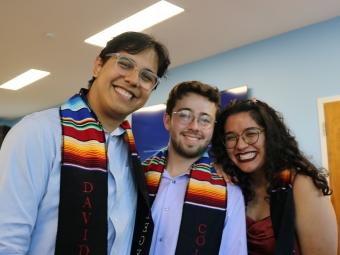 three Latinx students smile together while wearing graduation stoles