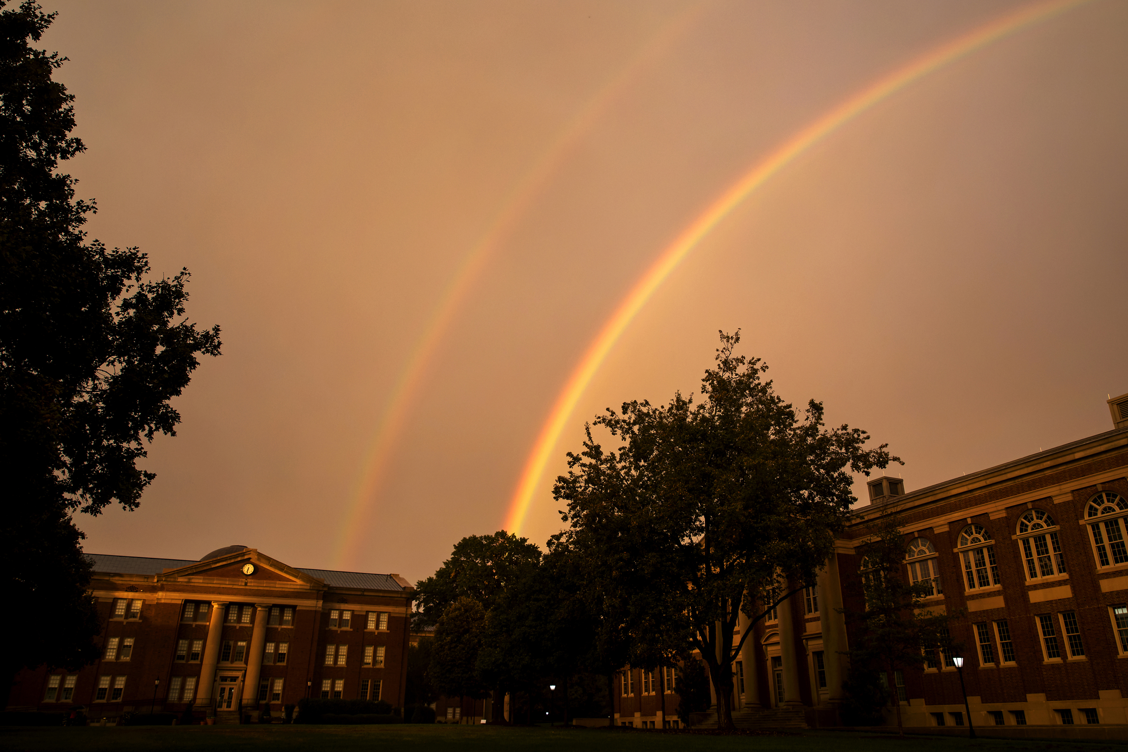 Sky rainbow over college buildings and trees 