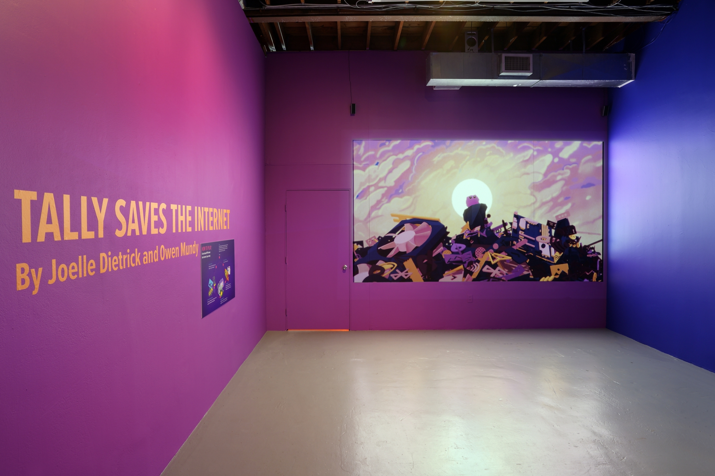 Tally Saves the Internet Exhibit text on wall in purple room, with screen projecting creature on pile of rubble