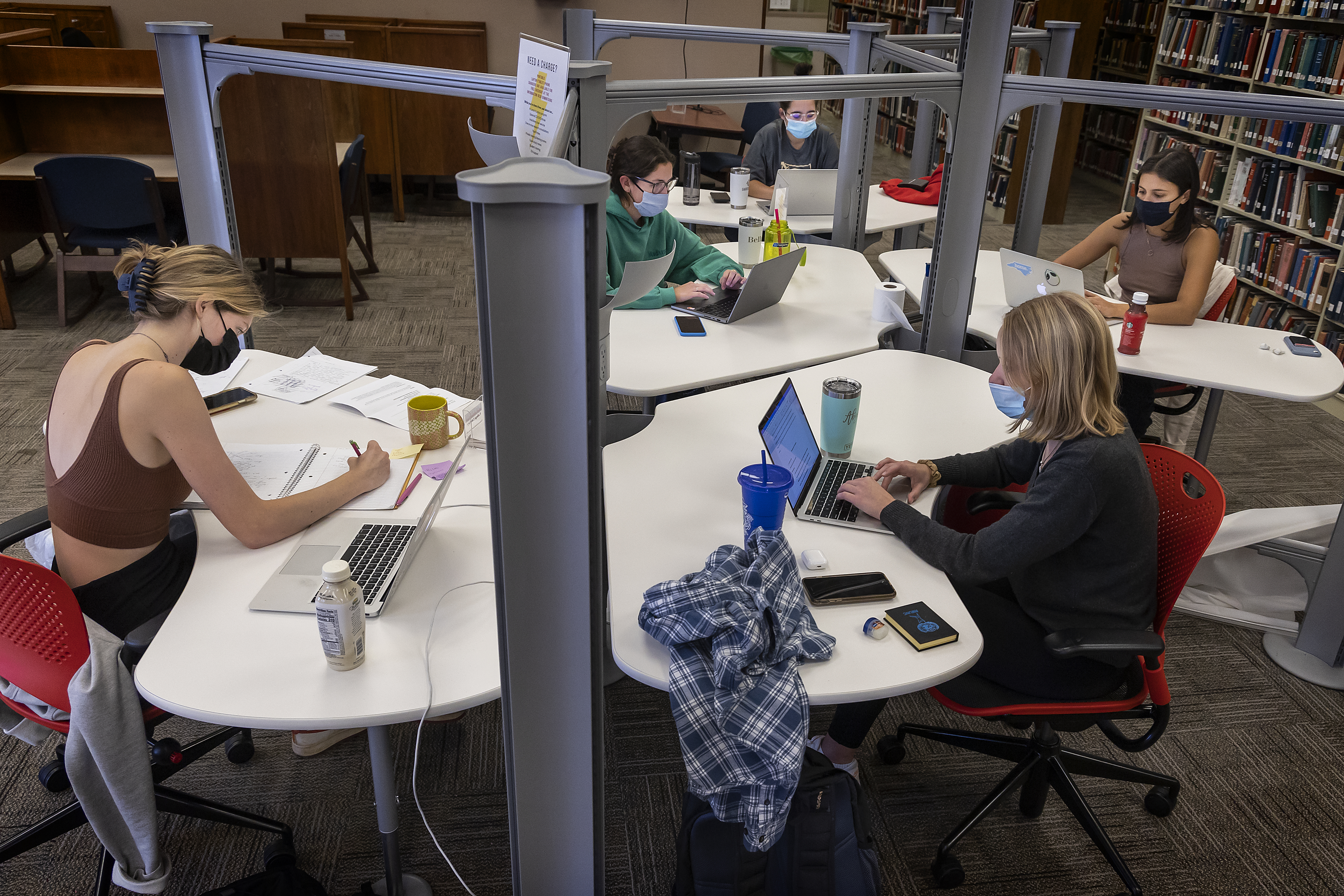 Group of students studying at pod of desks in library for final exams