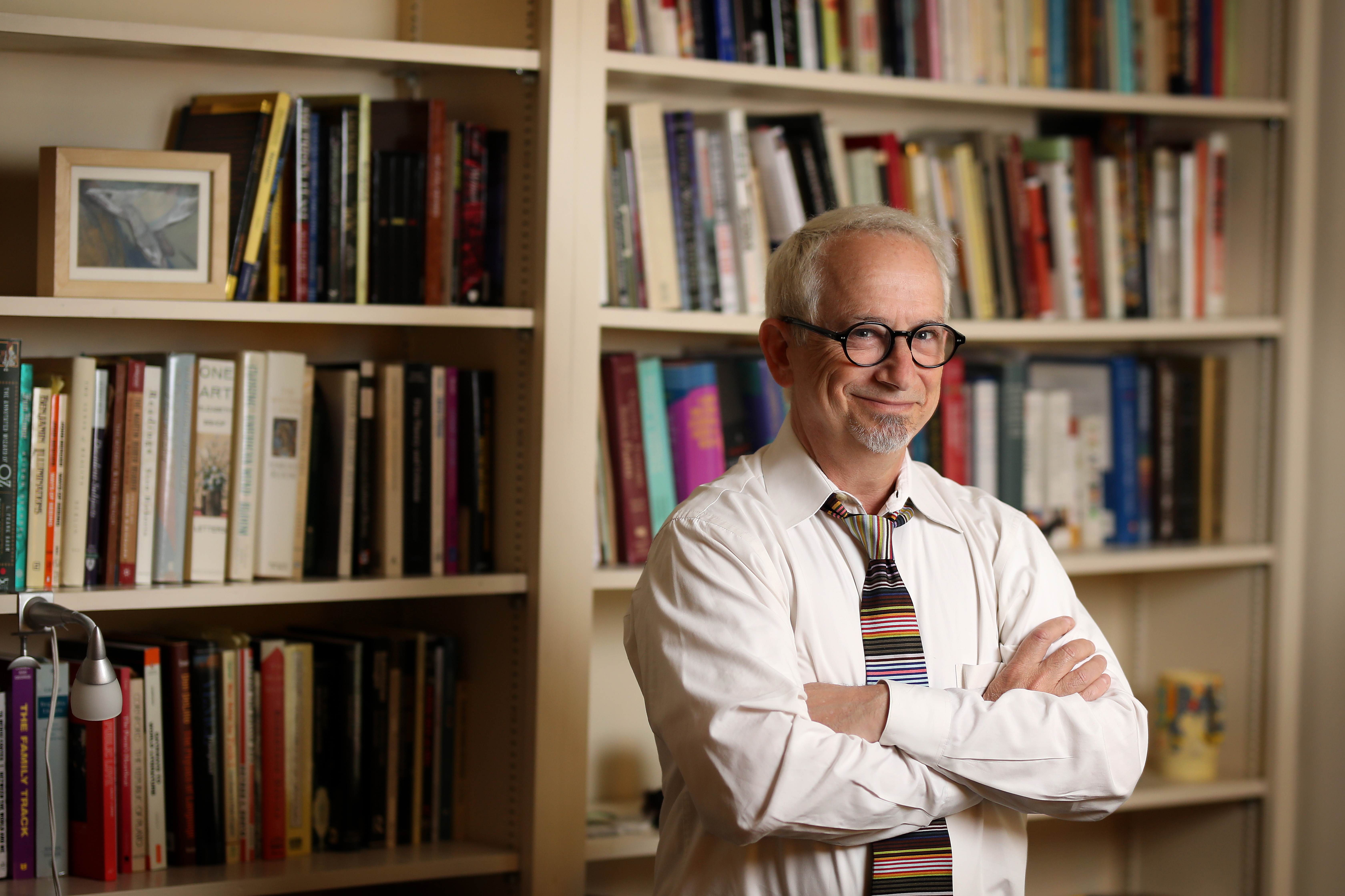 a middle aged white man standing in front of a bookcase smiling