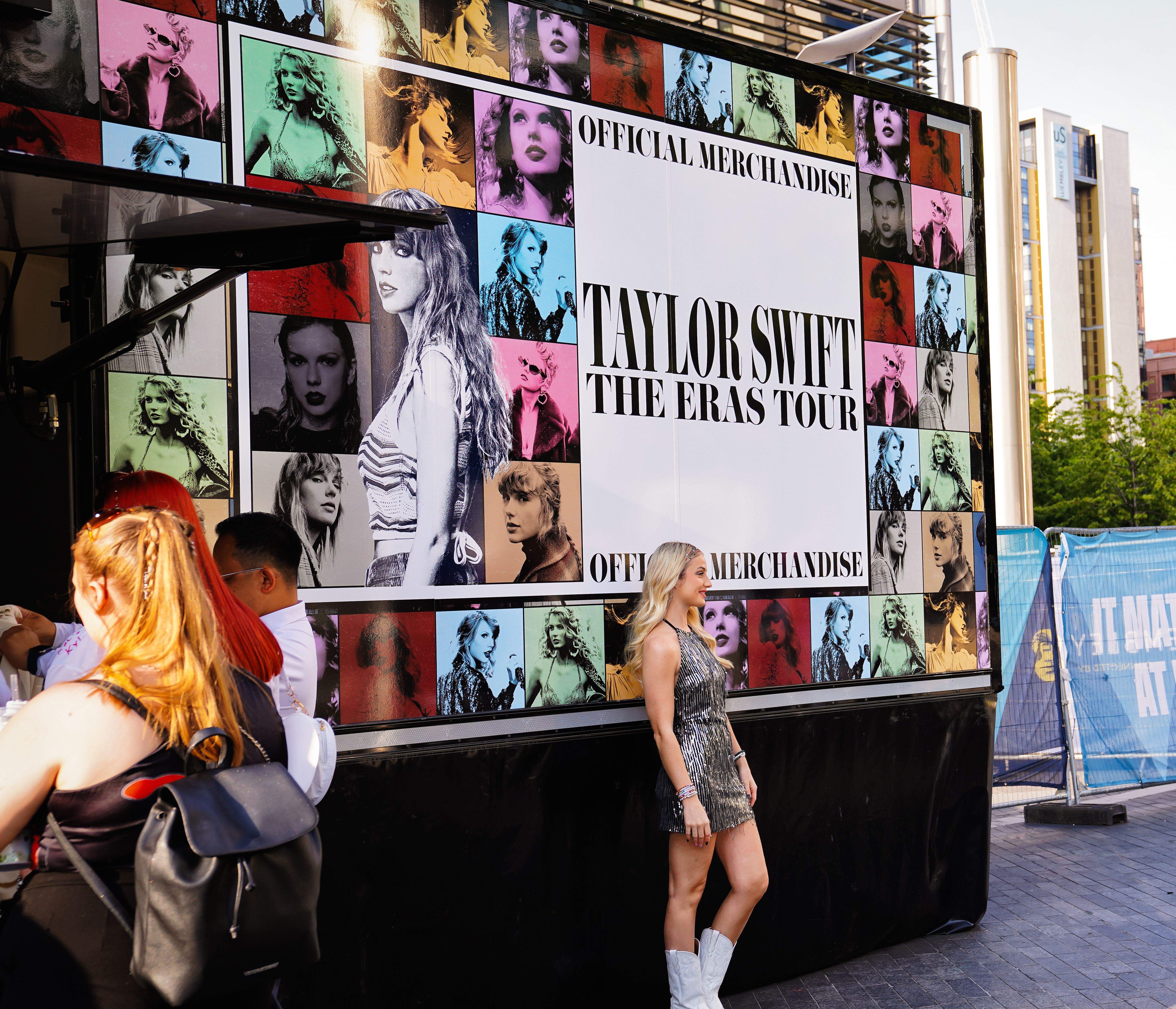 a young woman stands in front of sign that reads "Taylor Swift Eras Tour"