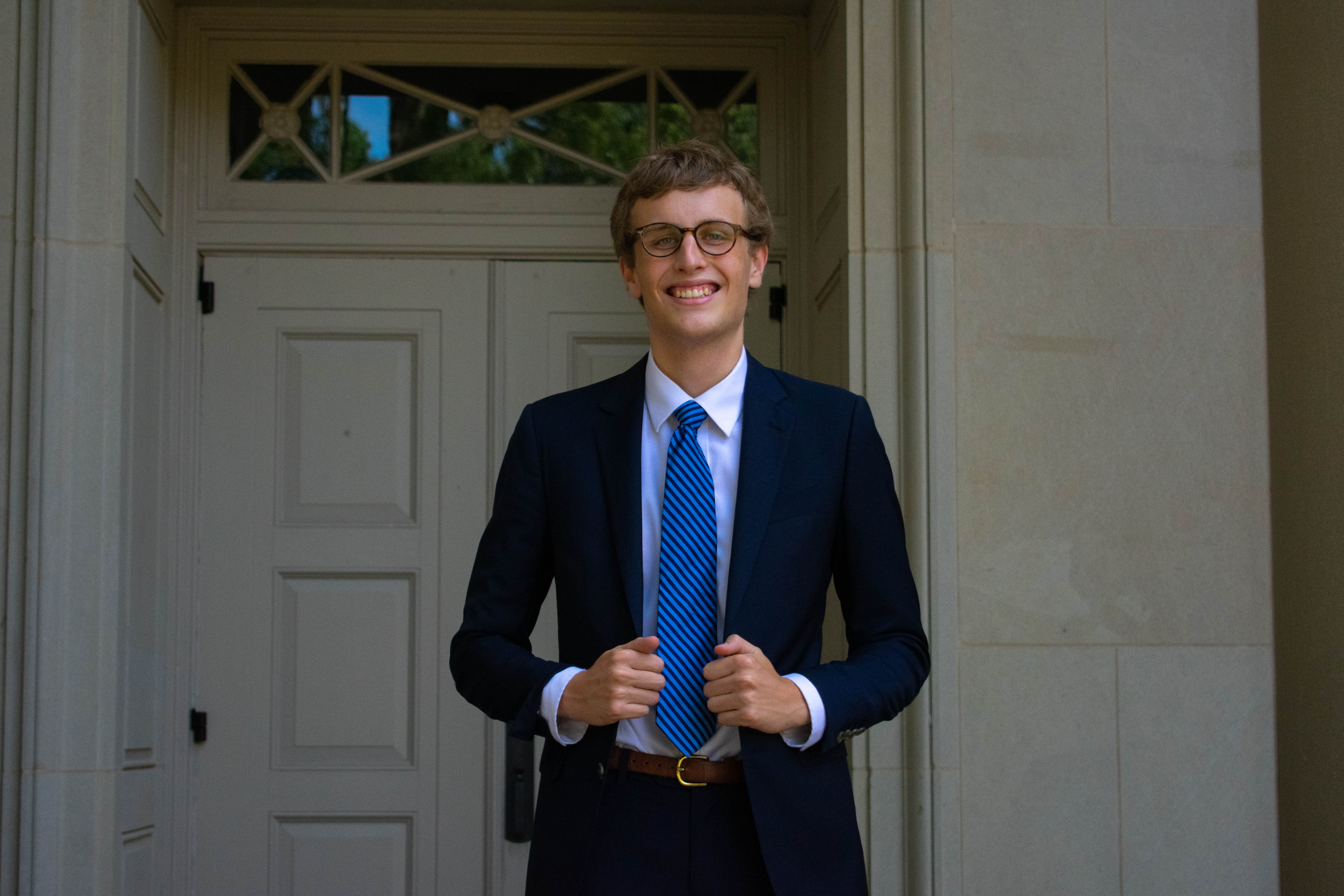 a young white man wearing a suit and tie standing in front of an old building