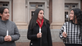 three young women walk together talking and holding candles