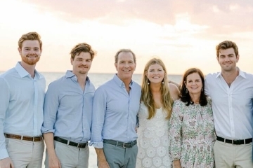 a family of six standing on a beach at dusk