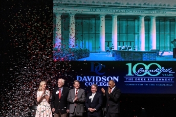 a group of five people standing on a stage clapping as confetti falls around them