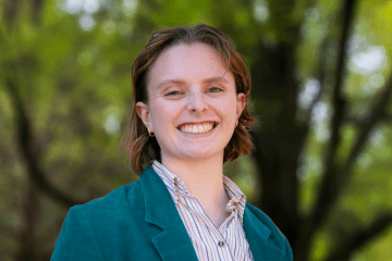 a young white woman wearing a collared shirt and jacket smiles