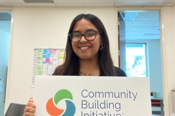 a young woman holds a sign that says "community building initiative"