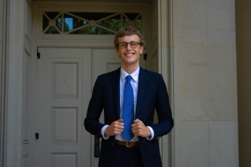 a young white man wearing a suit and tie standing in front of an old building