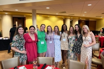 a group of young women in dresses and nametags smile standing together