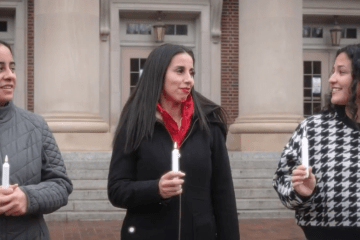 three young women walk together talking and holding candles