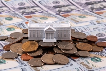 a plastic federal building sitting on a pile of coins and bills