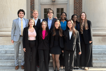 a group of young people in business formal clothing standing together in front of an academic building