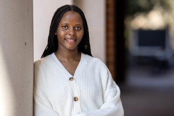 a young Black woman wearing a white sweater leaning against a column