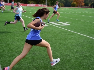 Flickerball game shows a student holding a football under her arm and running while others try to catch up to her