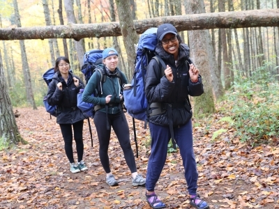 Three students backpacking in the woods walk in a line