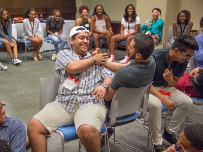 Two students sit next to each other during a team building game surrounded by other students