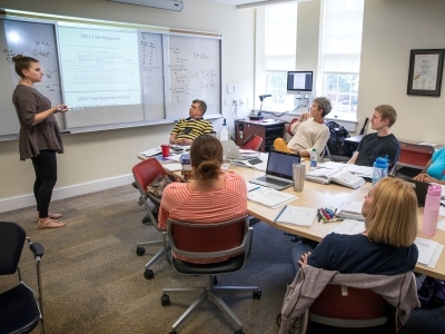 AP Summer Institute teachers gather around a table and engage in discussion with teacher standing by presentation