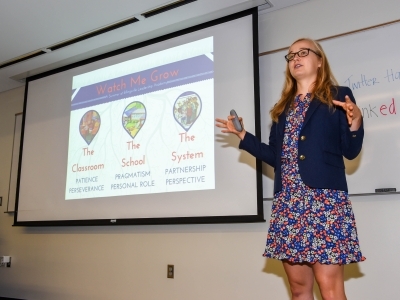 Student stands in front of presentation screen and presents to a room