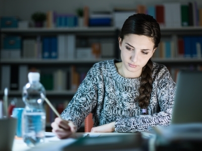 Student at computer writing books in background