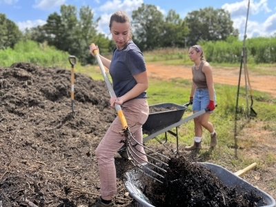 Students working at farm with pitchforks and wheelbarrows