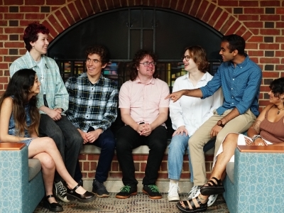 seven students sitting around a fireplace together talking and smiling