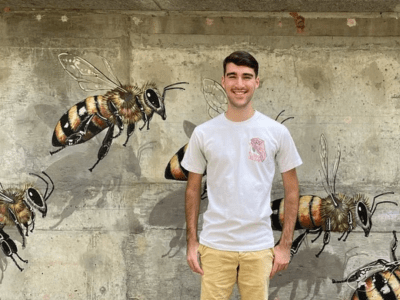 Student standing in front of bee mural