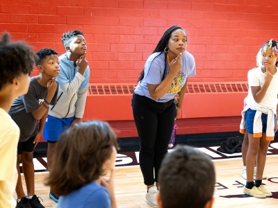 A young woman leads students in exercise in gym