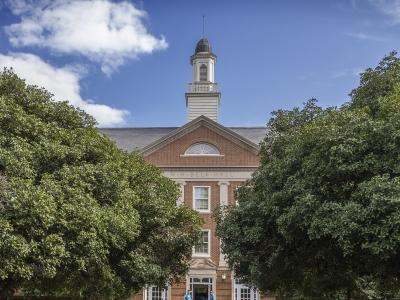 a brick building surrounded by green trees and blue skies in the background