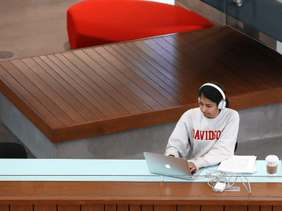 student wearing a Davidson sweatshirt and headphones works on a laptop in a modern academic building