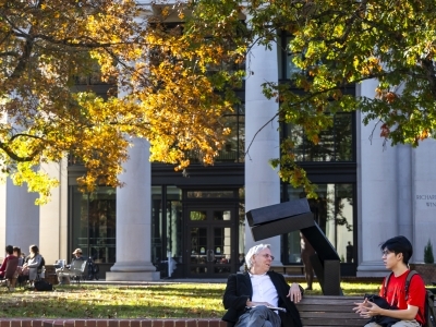 a faculty member and a student sit on a bench outside and have a conversation