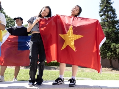 Two young women hold flags of various countries while smiling