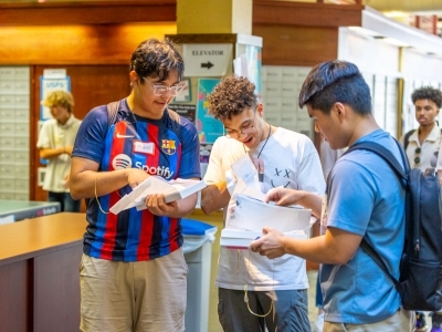 a group of three young men standing around and looking at a stack of papers