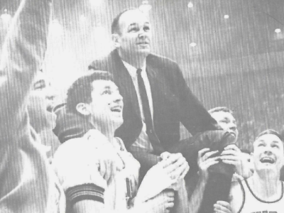 a men's basketball team holds a coach on their shoulders