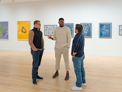 a group of three men stand together in an art gallery talking