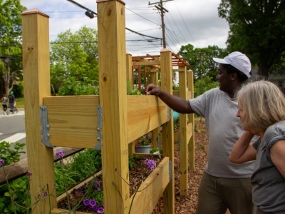 a young Black man talks to an older white woman around a community garden