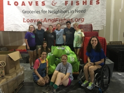 a group of students pose together in front of a "Loaves and Fishes" sign