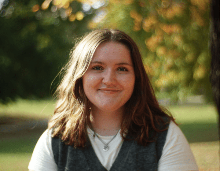 a young white woman wearing a tshirt and sweater vest outside