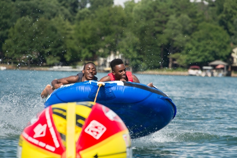 Two kids hang on to a tube as they are pulled across the water, laughing